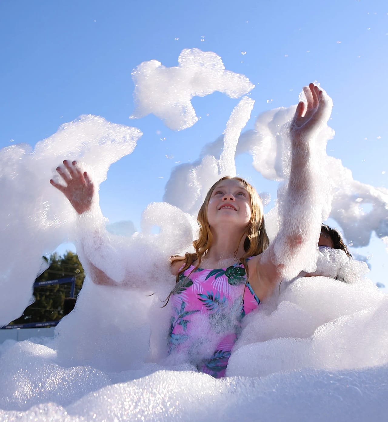 Girl looking up and throwing foam into the air against a bright blue sky at a foam party